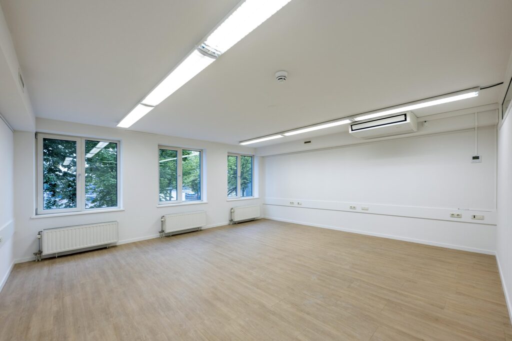 Leeg kantoorruimte met houten vloer, witte muren, grote ramen en ingebouwde verlichting aan de Prins Hendrikkade.